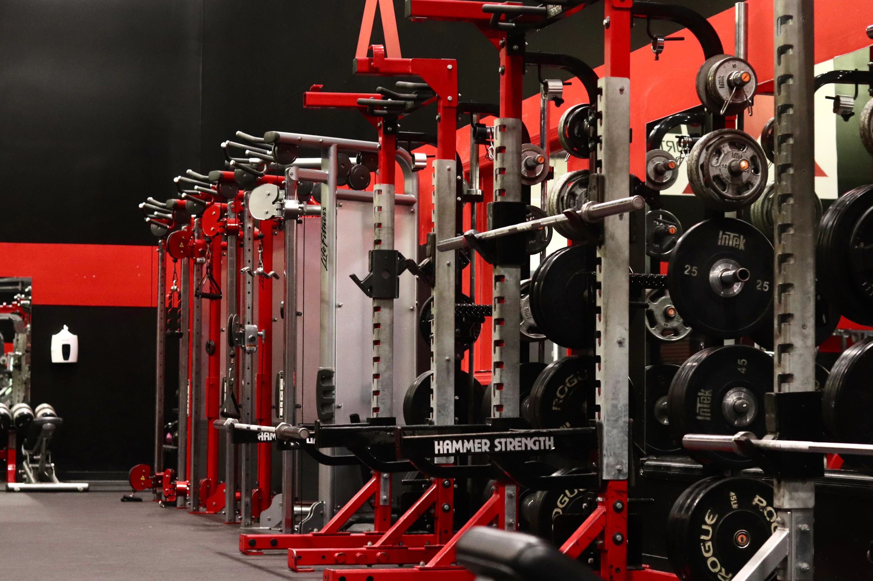 Row of Hammer Strength squat racks loaded with plates at XCEL Sports & Fitness, a gym in Fairfield, NJ