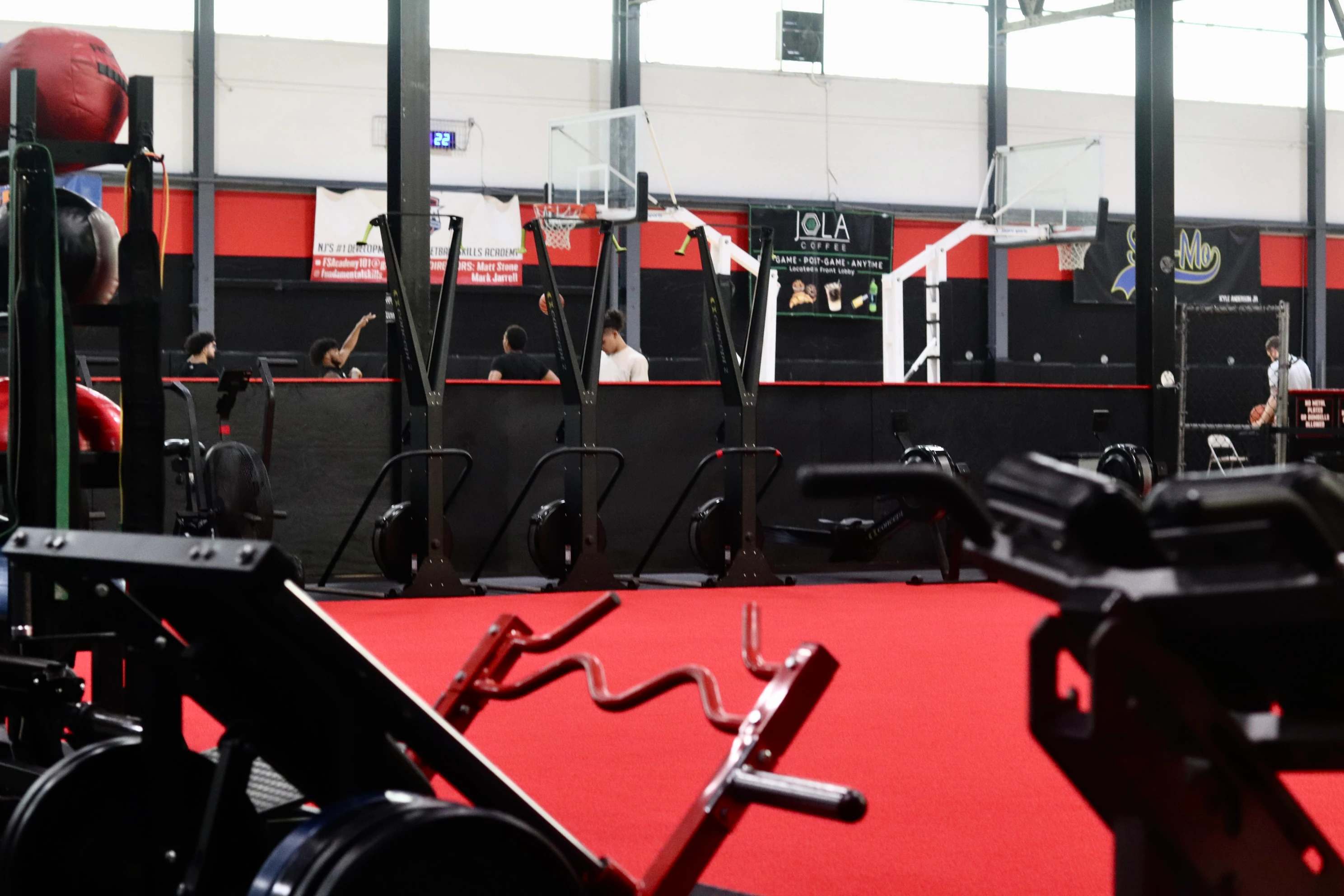 Sled and landmine on the red turf with athletes on the basketball courts behind at XCEL in Fairfield, NJ