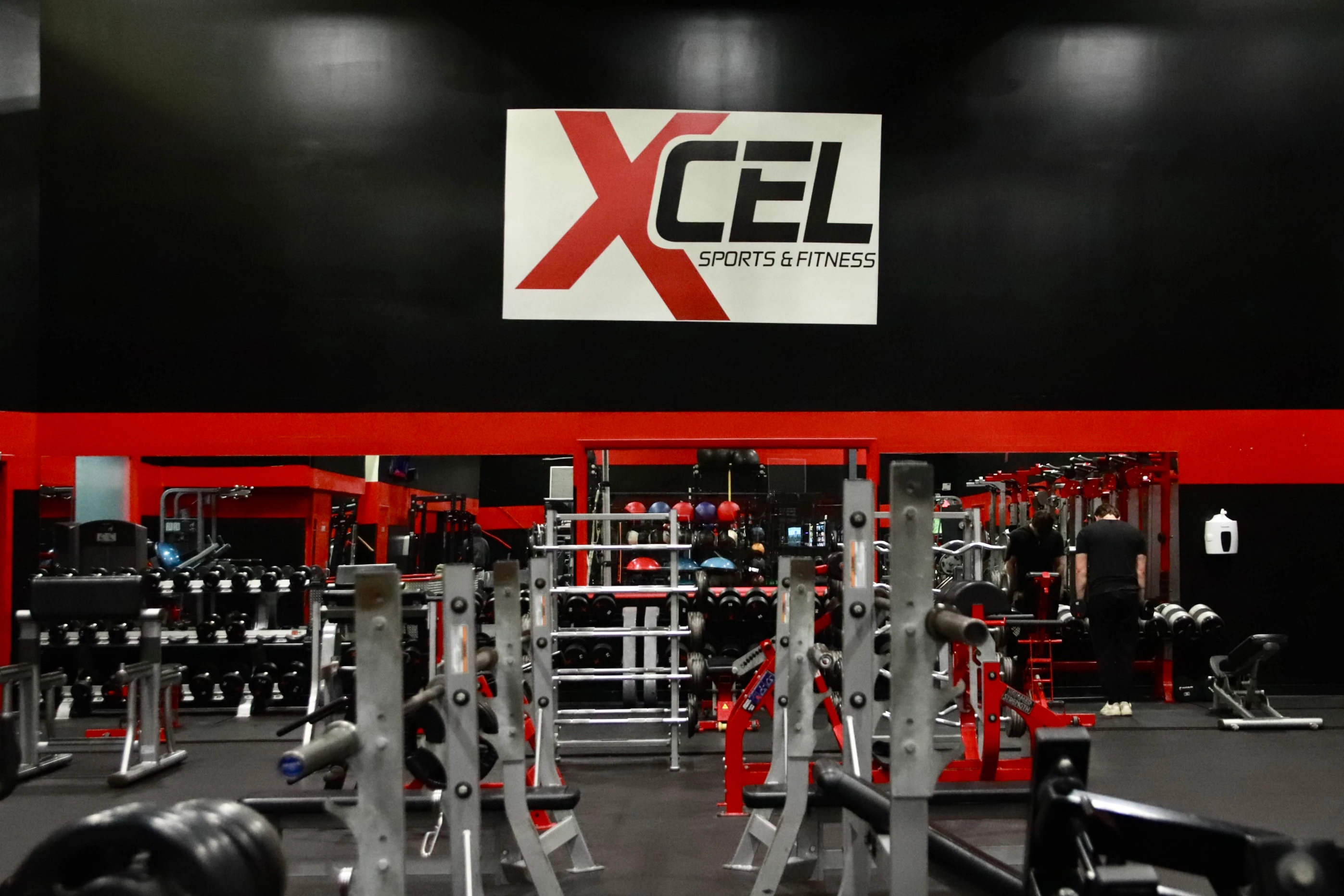 XCEL Sports & Fitness logo wall above the squat racks on the strength floor of the gym in Fairfield, NJ